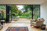 A lounge with bi-fold doors looking on to a contemporary city garden with gravelled seating area, raised lawn and garden room.