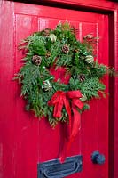 Christmas wreath  with pine cones berries and dried fruit and red bow on red door.