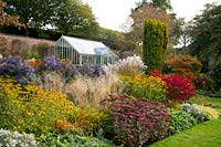 A glasshouse and herbaceous beds of Rudbeckia, Sedum, Asters, and Pennisetum in the walled garden at Holehird Gardens, Windermere, Cumbria, UK