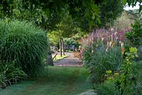 A grassy path leads between twin borders of miscanthus, red hot pokers, coneflowers and persicaria.