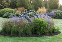 A contemporary sculpture by Ann Vrielinck in a central bed, surrounded by blue Russian Sage and orange Cosmos.
