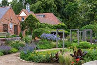 View into the contemporary lower garden where two small oval lawns, and a sinuous path straddled by an oak pergola, are enclosed in prairie style borders of Achilleas, Sea hollies, Catmint, Aconites, Campanulas, Salvias, Daylilies, Grasses and Verbenas