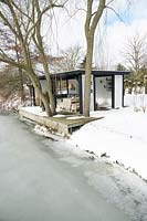 Summerhouse with comfortable lounge furniture on the edge of a frozen lake in the middle of a snow covered area
