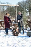 Man and wife Martijn and Liesbeth, warming their hands near the fire basket in the snow.