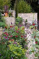 Stony path leading to walled terrace seating area with Dahlia coccinea 'Great Dixter', Verbena bonariensis and hollyhocks