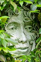 Ceramic face surrounded by foliage