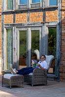 Woman sitting on patio reading with house behind