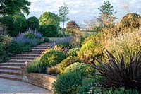 Steps leading up from terrace, mixed planting on slope includes: Phormium 'Bronze Baby' and Erigeron Sea Breeze'