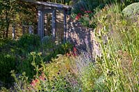 Garden on slope with flower bed in sun and shaded stone wall terrace and summerhouse
