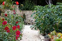 Stone path leading to a walled terrace seating area with Dahlia coccinea 'Great Dixter' and Datura stramonium