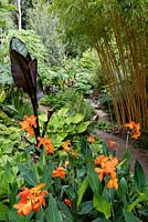 Canna 'Orange Punch' in an exotic garden, with path leading to a decked seating area. 
