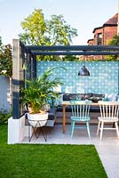 Dining area with colourful wall, chairs, modern pergola, industrial style lamp and the palm in the white pot.
