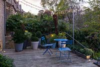 Low maintenance  city garden - night view of seating area with blue metal  bistro chairs