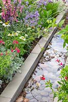Contemporary rill water feature lined with large pebbles next to colourful summer mixed border including Artemisia, Nepeta 'Six Hills Giant', Salvia 'Mirage Cherry Red' and Echinacea purpurea 'White Swan'. The Viking Cruises Lagom Garden - Hampton Court Flower Festival 2019