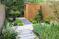View through modern London garden, to wooden shed surrounded by mixed planting and modern stepping stones with gravel infill, by Earth Designs. 