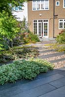 View over paved area in modern, North London garden, with Ebony Cloud schist paving with Japanese polished pebbles. 
