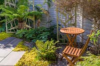 Paved sitting area with wooden bistro table and chairs, in modern, north London garden by Earth Designs.
