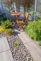 Paved sitting area with wooden bistro table and chairs, in modern, north London garden by Earth Designs.
