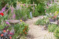 View along a crushed stone pathway through a wildlife friendly garden with stone bird bath. Springwatch Garden, Hampton Court Flower Show, 2019.
