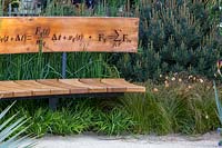Curved bench seat decorated with mathematical symbols cut into band of copper forming back. The Winton Beauty of Mathematics Garden. The RHS Chelsea Flower Show, 2016. Sponsor: Winton.