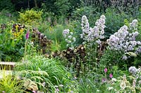 Naturalistic borders of perennials and ornamental grasses with wildlife friendly log piles.