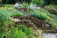 Insect and wildlife friendly log walls within naturalistic borders planted with perennials.
