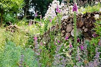 An insect and wildlife friendly log wall within naturalistic borders planted with foxgloves, alliums and catmint.
