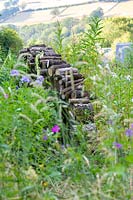 An insect and wildlife friendly log pile within a naturalistic border planted with perennials and ornamental grasses.