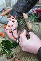 Woman wiring rose hips, pine and pinecone to twig wreath. 