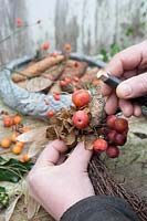 Woman adding colourful crab apples to wreath. 