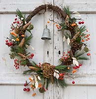 Pine wreath using berries, cones, flowers and a metal bell, hanging on a rustic wooden door