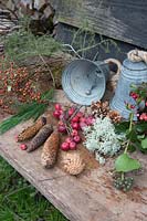 Materials for making a rustic Christmas wreath including rosehips, crab apples, pinecones and foliage hanging from two metal bells. Styling by Marieke Nolsen. 