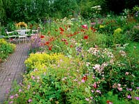 Mixed colourful flower borders with view to white table and chairs in the background. 

