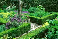 Traditional water tap in formal garden with clipped Buxus hedges surrounding mixed flowerbeds.