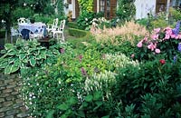 View over flower bed with Astilbe, Geranium vivace, Hosta and Salvia nemorosa beyond seating area and house