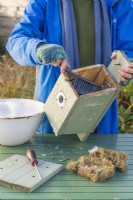Woman using a brush with disinfectant and water to clean out a bird box in Winter ready for birds to use for nesting