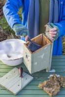 Woman using a brush with disinfectant and water to clean out a bird box in Winter ready for birds to use for nesting
