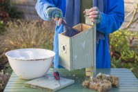 Woman using a brush with disinfectant and water to clean out a bird box in Winter ready for birds to use in Spring