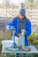 Woman using a brush with disinfectant and water to clean out a bird box in Winter ready for birds to use in Spring