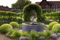 Herb garden at Arundel Castle, West Sussex in May, with water feature surrounded by clipped box, clumps of chives and thymes, fennel and trained apples underplanted with purple sage