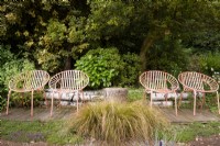 A quartet of orange metal garden seats surrounded by lush planting including evergreen shrubs such as Prunus laurocerasus and hollies, orange sedge Carex testacea and creeping thymes in a cottage garden in June