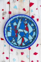 Mosaic bird bath on wooden surface surrounded by pieces of smashed plate