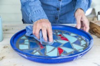 Woman using a damp cloth to wipe off any excess grout from the mosaic