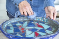 Woman wiping grout off of the surface of the mosaic tiles