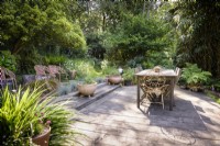Simple decked dining area surrounded by dense trees and shrubs in a country garden in June.