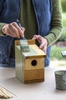 Woman using a paintbrush to paint a bird box