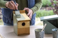 Woman using a paintbrush to paint a bird box