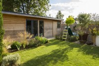 Modern wooden outbuilding with lawn children's play area with colourful slide in modern family garden 