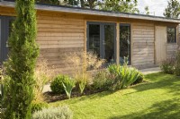Lawn and border in front of wooden outbuilding in modern family garden 