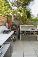 Outdoor kitchen with red pizza oven and  hob with built-in wood storage in small modern family garden